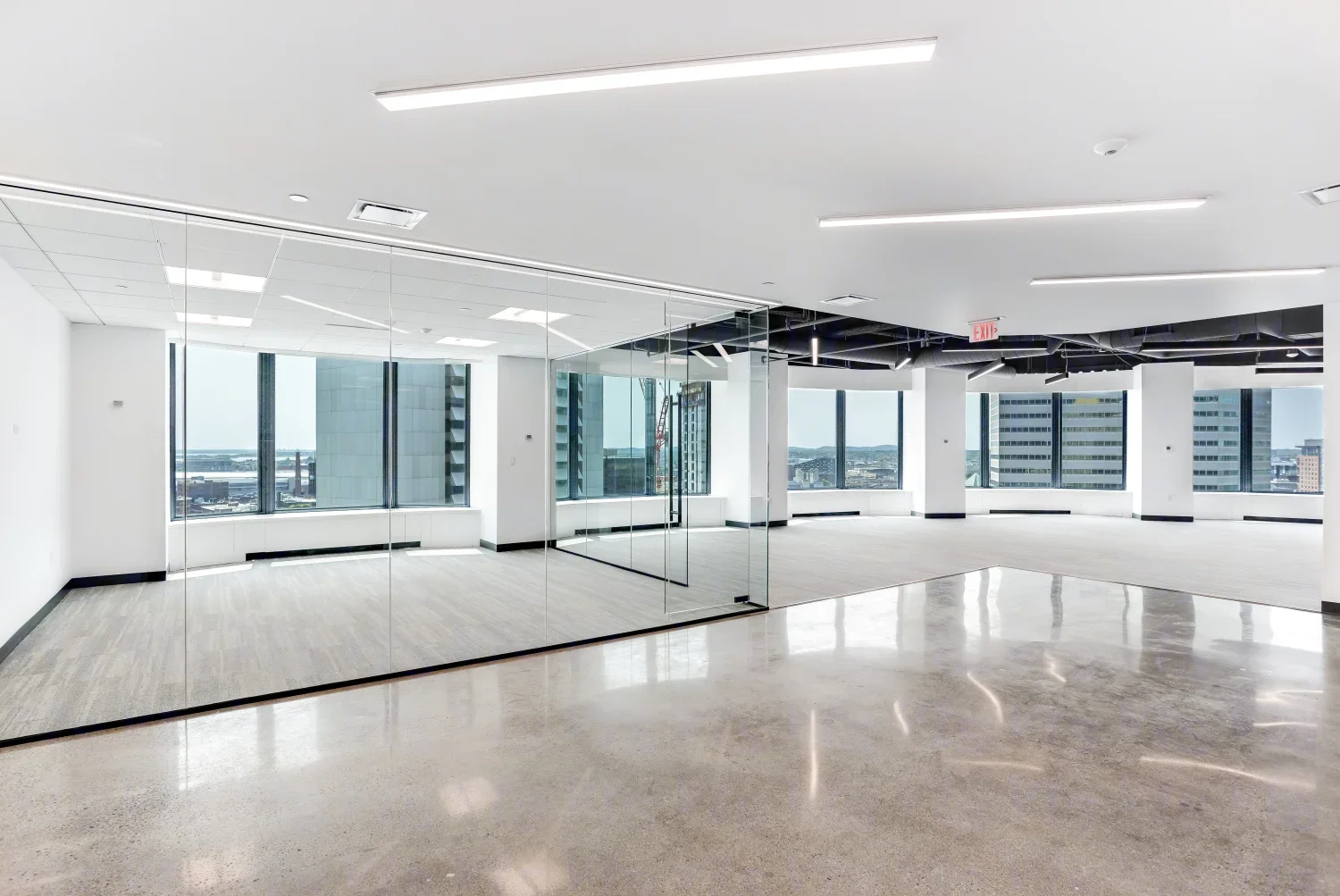 Bright, modern office space featuring glass partitions, polished concrete floors, and large windows overlooking a city skyline.