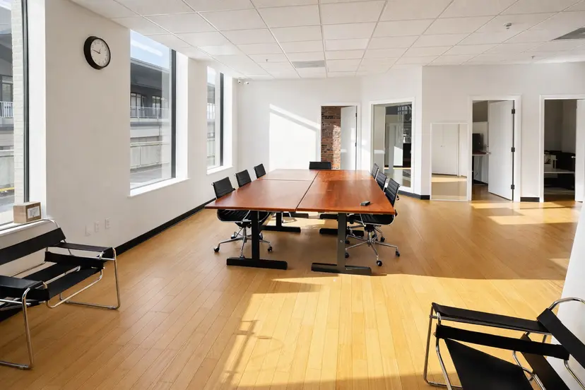 Bright conference room with large meeting table, natural light, and private offices in modern workspace
