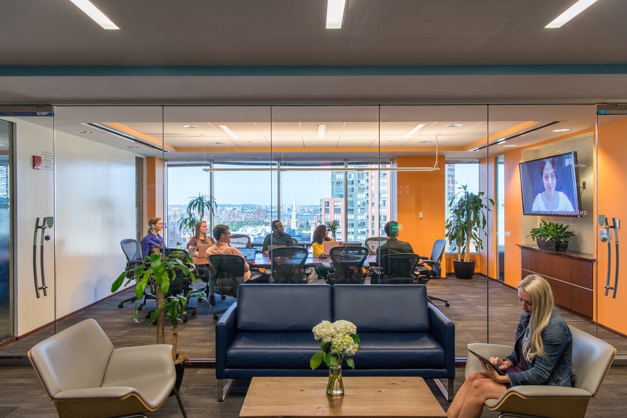 Modern office conference room with team meeting behind glass walls and city skyline views
