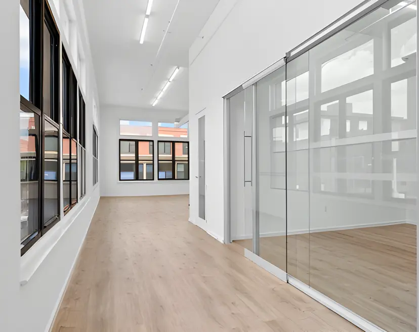 Bright modern office space with glass meeting room, hardwood floors, and large windows