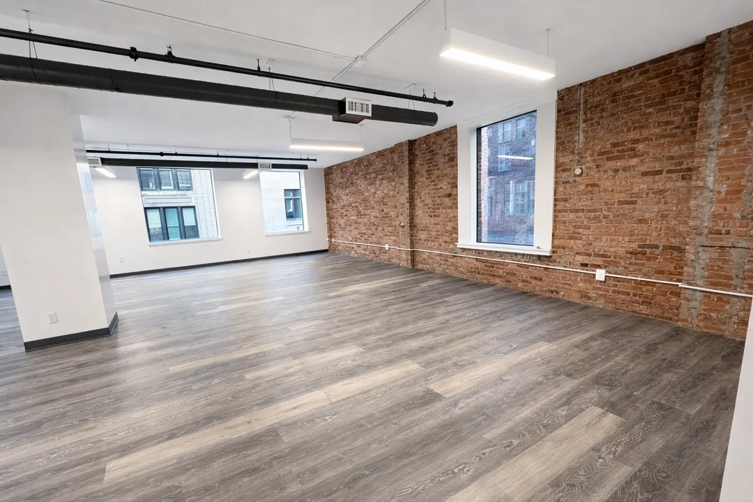 Open industrial-style office interior featuring exposed brick walls, modern lighting, and wide plank flooring.