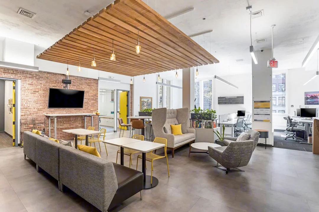 Contemporary office common area featuring soft seating, wood slat ceiling detail, exposed brick, and collaborative workspaces.