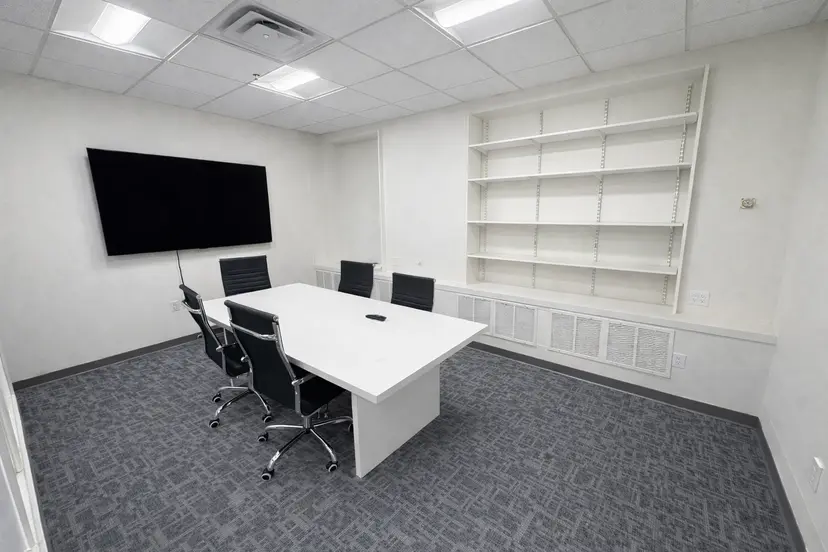Small private meeting room with conference table, wall-mounted screen, and built-in shelving