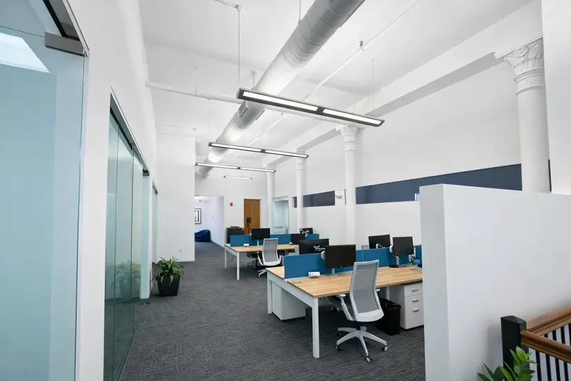 Modern open office workspace with shared desks, glass offices, and high ceilings